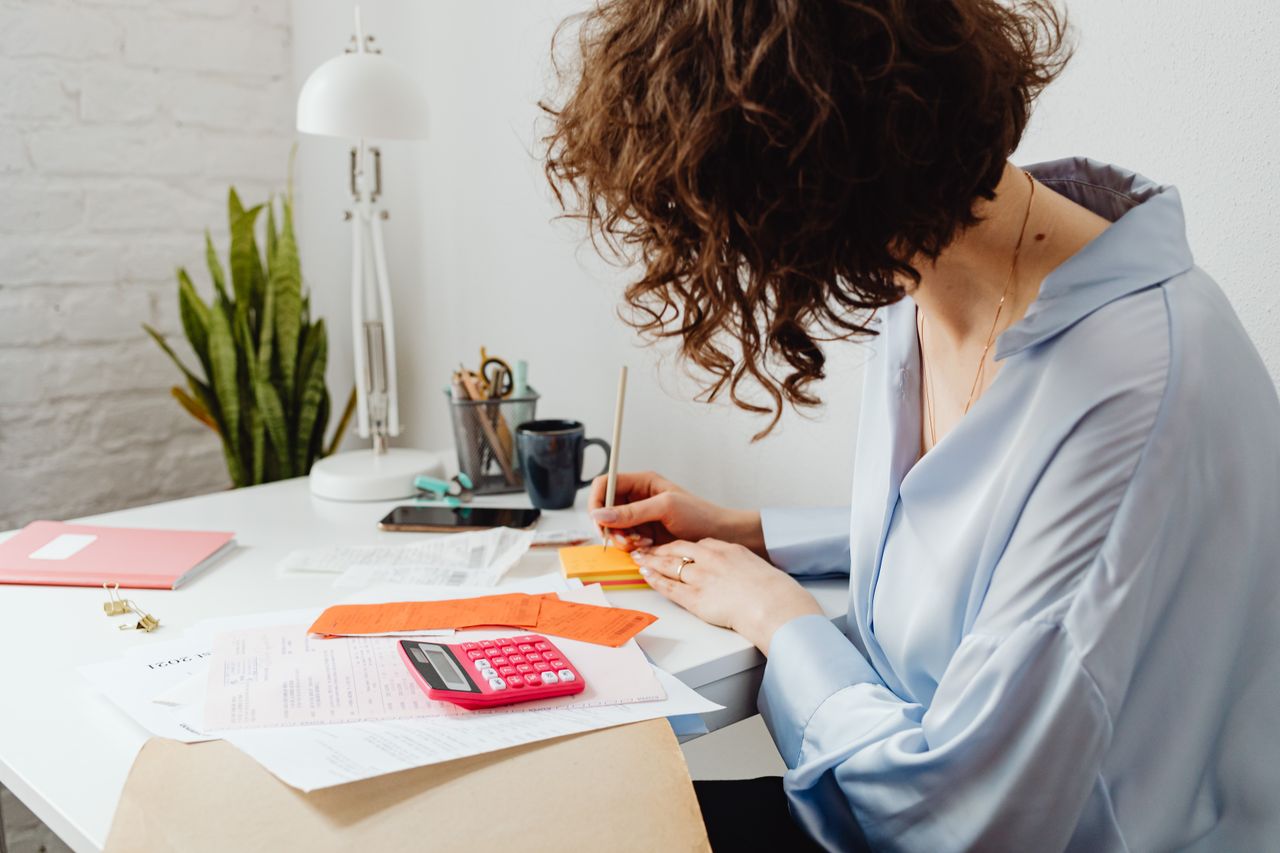 Woman writing with calculator on desk, managing finances indoors.